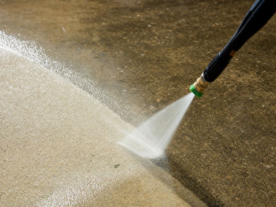 A pressure washer clearing years of grime from a concrete driveway